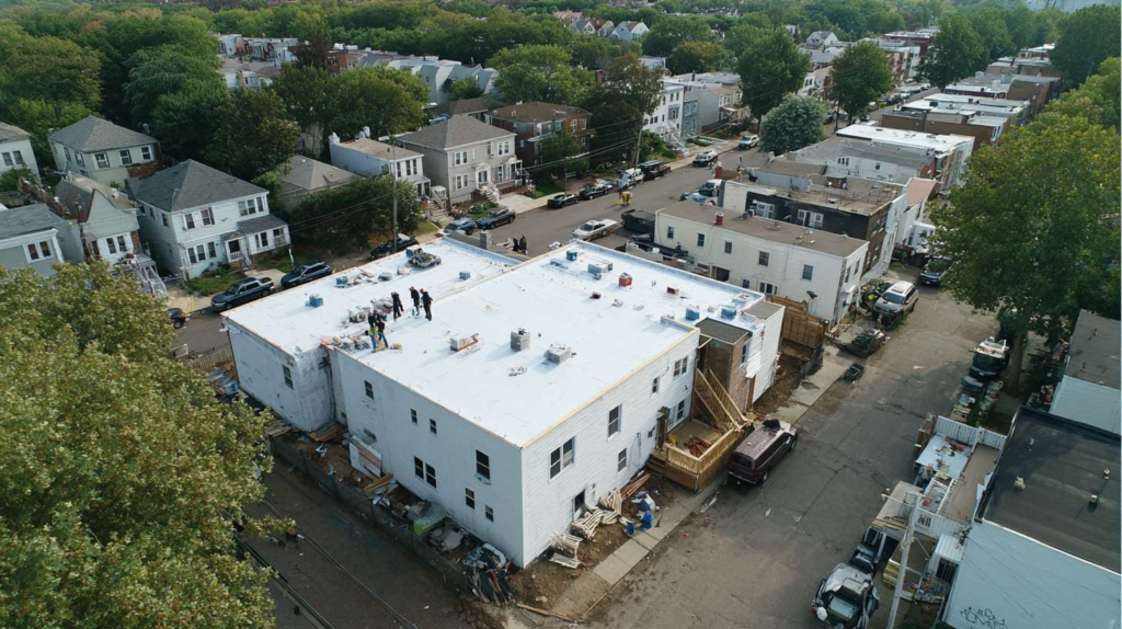 A flat roof installation showing rubber membrane roofing material being applied over a commercial building with urban skyline in background.